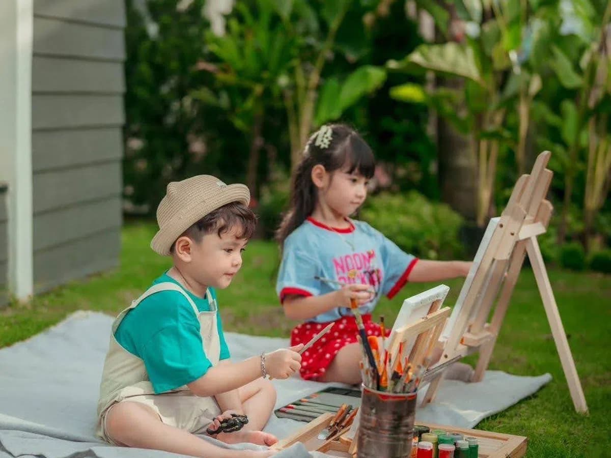 Hai bé vẽ tranh trên bãi cỏ trước căn nhà tại Home Retreat